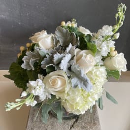 White roses and hydrangeas in a glass vase with silver foliage