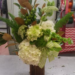 Tall floral arrangement with white hydrangeas and green accents in a wooden vase