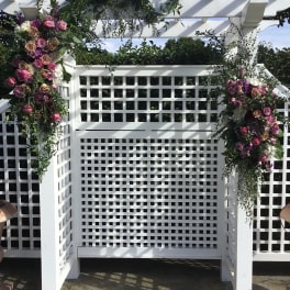 Floral arrangements of pink and purple roses on a white pergola arch