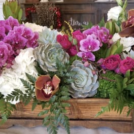 Mixed floral arrangement in a wooden box with orchids, roses, and succulents