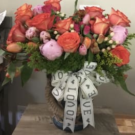 Bouquet of orange roses and pink peonies in a woven vase with a LOVE ribbon