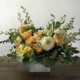 Yellow and white floral arrangement in a clear square vase
