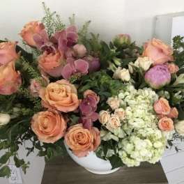 Mixed bouquet of peach roses, pink orchids, and pale hydrangeas in a white vase