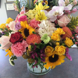 Mixed bouquet of roses, lilies, orchids, and sunflowers in a glass vase