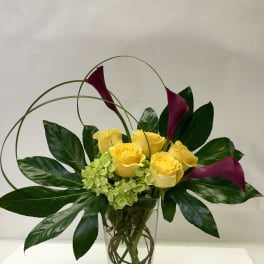 Yellow roses and purple calla lilies in a clear glass vase