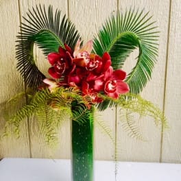 Red orchid arrangement in a tall green vase with palm fronds