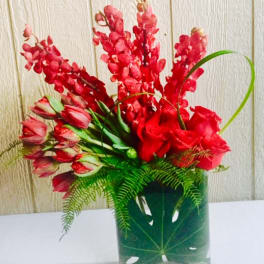 Red floral arrangement in a clear square vase with fern foliage