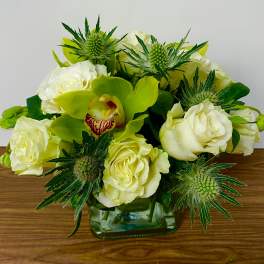 White roses and a green orchid arranged in a square glass vase