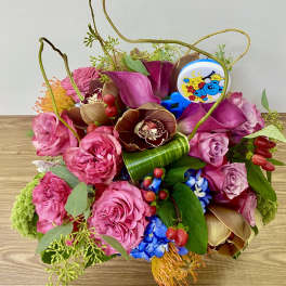 Pink and purple floral arrangement with orchids and roses in a low container