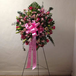 Pink and white funeral spray on a stand with a large pink ribbon