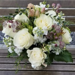 White rose bouquet with small purple flowers in a clear vase