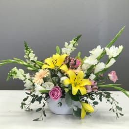 Mixed bouquet with yellow lilies, pink roses, and white snapdragons in a white bowl vase