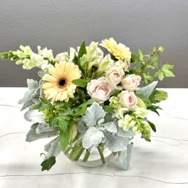 Mixed bouquet of pale roses, gerbera daisies, and white blooms in a glass vase