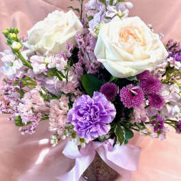 Bouquet of white roses and purple flowers in a vase with a pink ribbon
