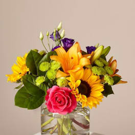 Mixed bouquet in a clear glass vase with pink rose, lilies, and sunflowers