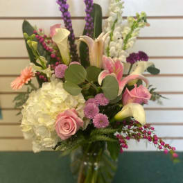 Mixed bouquet with pink roses, white hydrangea, and calla lilies in a glass vase
