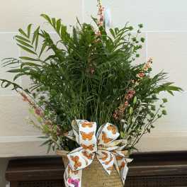Tall greenery arrangement in a woven basket with a butterfly ribbon