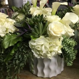 White floral arrangement with calla lilies, roses, and hydrangeas in a white vase