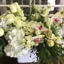 Large white floral arrangement with roses, orchids, and hydrangeas in a white container