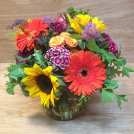 Mixed bouquet with sunflowers, gerbera daisies, roses, and carnations in a glass vase
