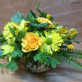 Yellow floral arrangement in a glass vase with mixed blooms