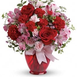 Red and pink flower bouquet in a red vase with a ribbon