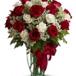 Red and white roses in a clear glass vase with a red ribbon