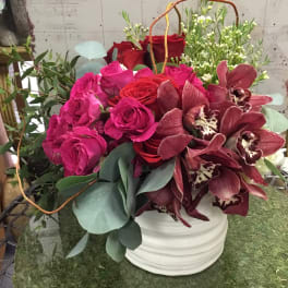 Bouquet of pink and red roses with burgundy orchids in a white vase
