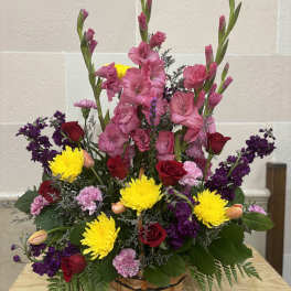 Basket arrangement of pink gladiolus, red roses, yellow mums, and purple flowers