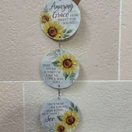 Three round sunflower plaques with Bible verse text hang vertically on a wall.