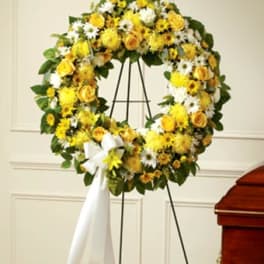 Yellow and white floral wreath on a stand with a white ribbon