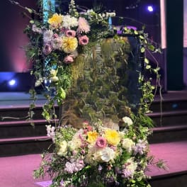 Large floral arrangement with pastel blooms and trailing greenery on a stand