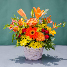 Mixed bouquet in a woven basket with orange, yellow, and red flowers