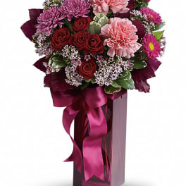 Bouquet of pink and red flowers in a tall purple vase with a ribbon