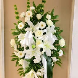White floral standing spray with lilies, daisies, and ribbon on an easel