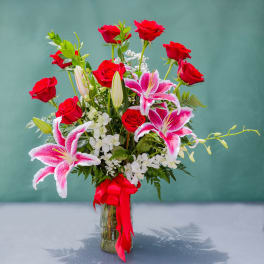 Red roses and pink lilies in a glass vase with a red ribbon