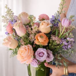 Pastel mixed bouquet of roses, tulips, and purple flowers in a glass vase