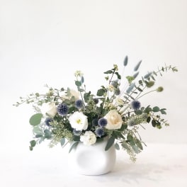 White and cream flowers in a round white vase with blue thistle-like blooms