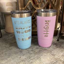 Two insulated tumblers with gold lids, one blue and one pink, with text on the front.