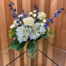 Blue hydrangeas with white roses and tall blue delphinium in a clear patterned glass vase