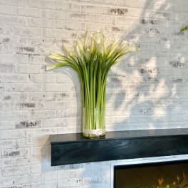 Tall bouquet of white calla lilies in a clear glass vase