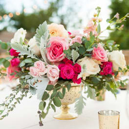 Pink and white roses arranged in a gold pedestal vase on a table