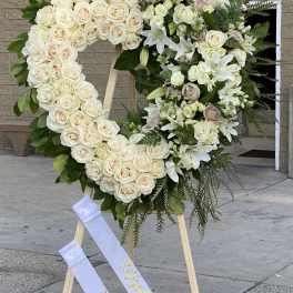 Heart-shaped floral wreath of white roses and lilies on an easel