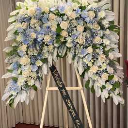 Large funeral wreath of white and blue flowers on an easel