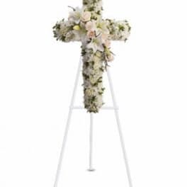 Floral cross arrangement on a white easel with pale blooms
