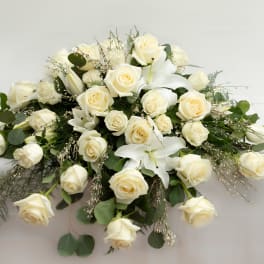 White rose and lily arrangement with greenery on a white surface