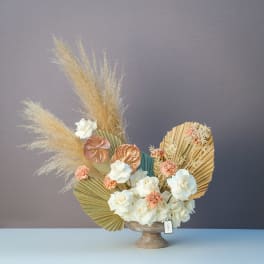 White roses and peach carnations in a pedestal vase with dried pampas grass