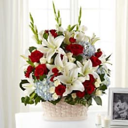 Basket arrangement of red roses, white lilies, and blue hydrangeas