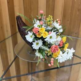 Bouquet of white daisies, yellow roses, and pink flowers in a wicker horn-shaped holder