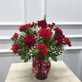 Red roses and carnations in a red glass vase with a patterned ribbon